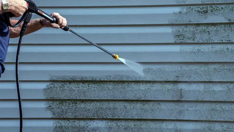 A person pressure washing the siding of a home.
