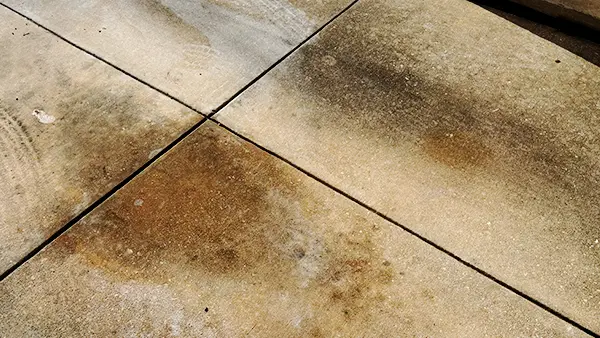 Concrete driveway with dark brown oil stains across several slabs.